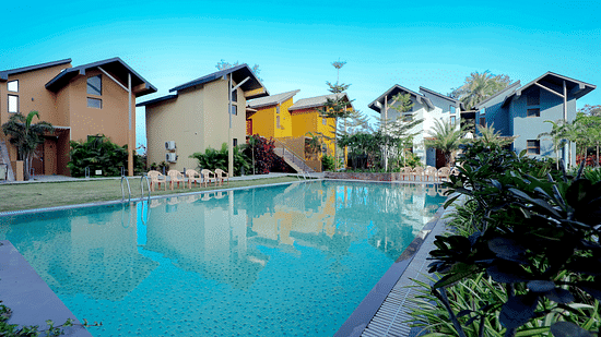 An image of a swimming pool surrounded by houses and trees - Pride Resort Ambaji